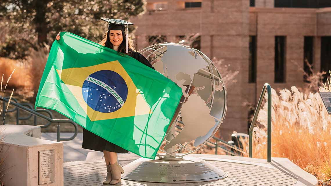 Student in cap and gown holding up the flag of Brazil
